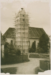 1954-1955. Der Kirchturm ist eingerüstet zur Renovierung. Vorn rechts liegen die neuen Dachplatten. Man beachte das alte Kirchendach mit Streifen nach der Umdeckung des Unwetters im Jahr 1929 (4.7.1929)